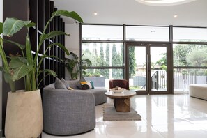 A modern living room with a sectional sofa, a round coffee table, and large potted plants. - Quao Realty - One Elm (Accra)