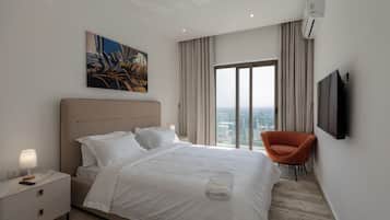 A hotel room with a bed, a nightstand, a lamp, a painting, a chair, a TV, and a view of the city through the window.
