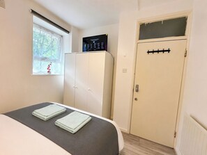 Un dormitori amb un llit, un armari, una finestra petita que dona a una vista i un termòstat a la paret.
