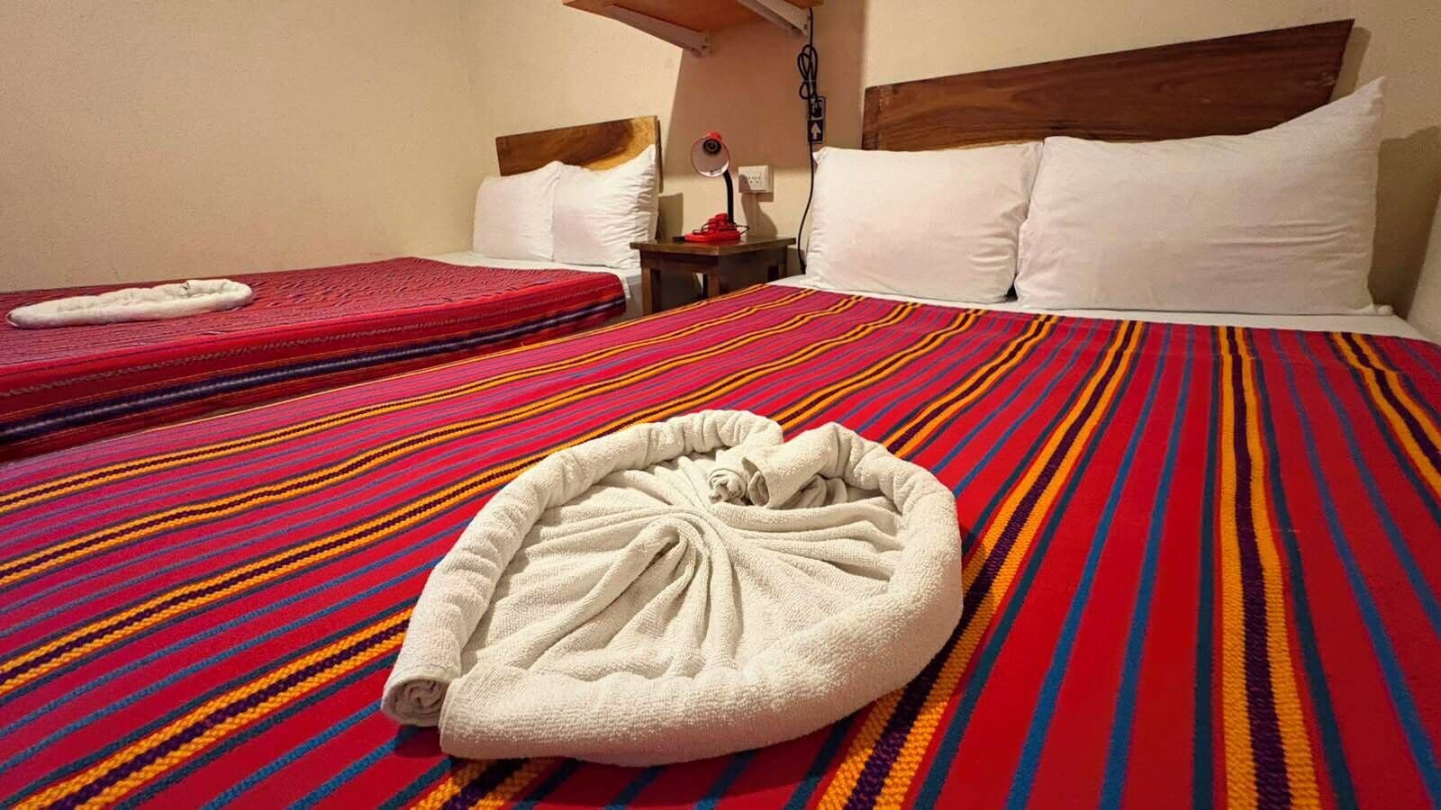 A hotel room with a bed, a bedside table, and a red and blue striped blanket.