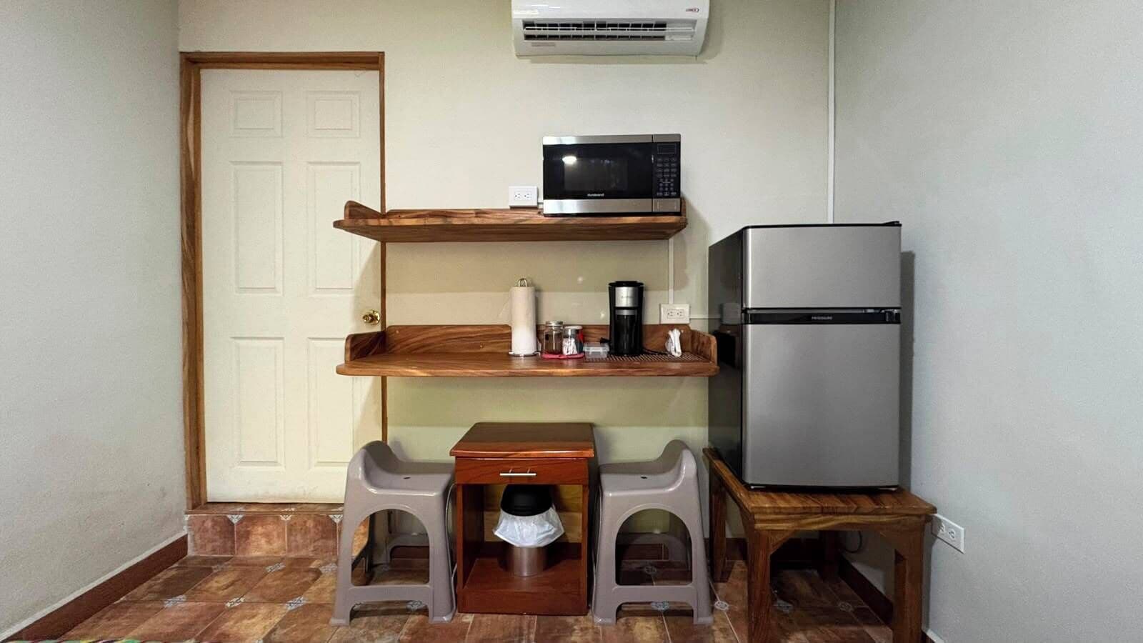 A compact kitchenette with a microwave, refrigerator, and a small table with stools.