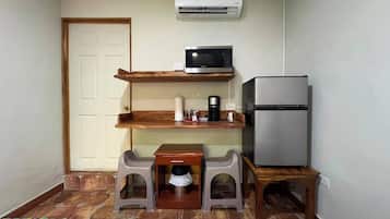 A compact kitchenette with a microwave, refrigerator, and a small table with stools.