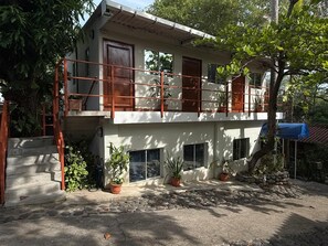 A two-story building with a balcony, potted plants, and a staircase leading to the entrance.