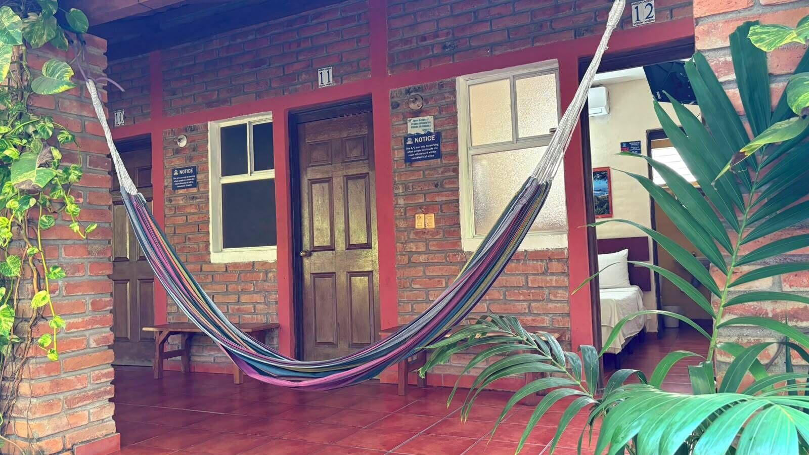 A brick building with a hammock in front, a door labeled '11', and a plant to the right.