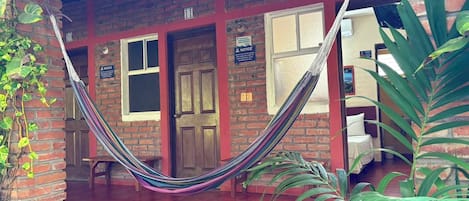 A brick building with a hammock in front, a door labeled '11', and a plant to the right.