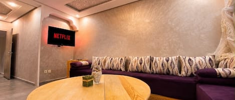 Un salon moderne avec une table en bois, un canapé violet et un téléviseur fixé au mur qui affiche « NETFLIX ».