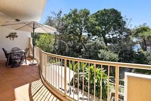 A balcony with a table and chairs, surrounded by a railing, overlooking a garden with various plants and trees. - Deluxe Three-Bedroom Apartment Apt 8 (Mooloolaba, Sunshine Coast)