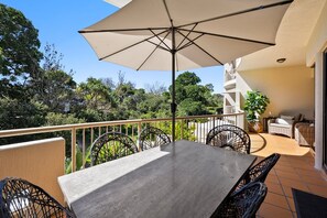 A balcony with a table and chairs, a large umbrella, and a view of greenery. - Deluxe Three-Bedroom Apartment Apt 8 (Mooloolaba, Sunshine Coast)