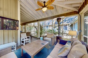 A covered outdoor seating area with wooden furniture, a ceiling fan, and large windows. - 2 Private Wings, Great Outdoor Spaces, Secluded Maritime Forest, Dogs OK, BHI Club + Golf (Bald Head Island)