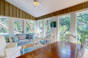 A room with a wooden ceiling, large windows, a dining table, and a sofa with cushions. - 2 Private Wings, Great Outdoor Spaces, Secluded Maritime Forest, Dogs OK, BHI Club + Golf (Bald Head Island)