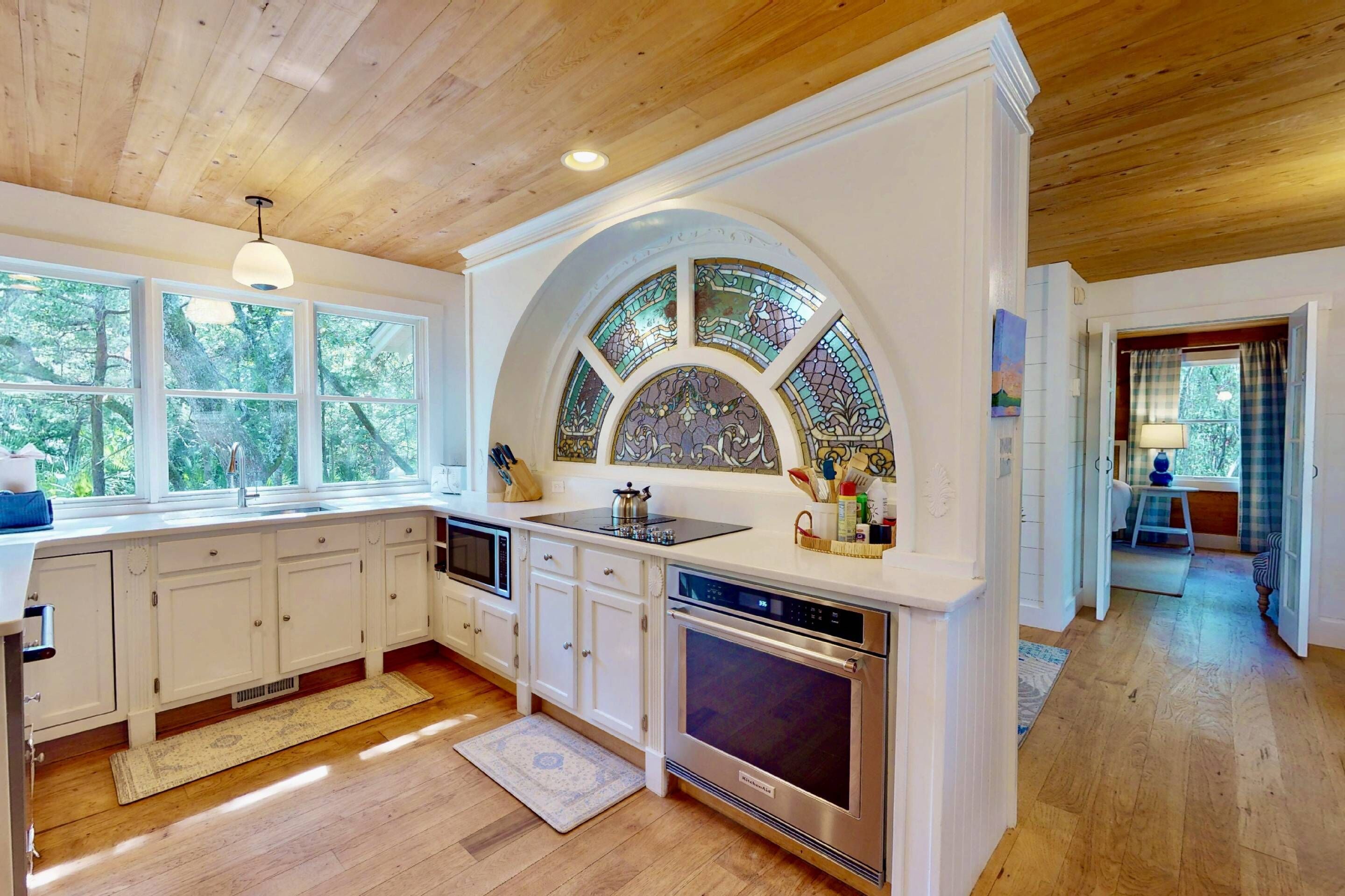 A kitchen with white cabinets, a large island, a built-in oven, and a stained glass window above the sink.