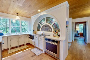 A kitchen with white cabinets, a large island, a built-in oven, and a stained glass window above the sink. - 2 Private Wings, Great Outdoor Spaces, Secluded Maritime Forest, Dogs OK, BHI Club + Golf (Bald Head Island)