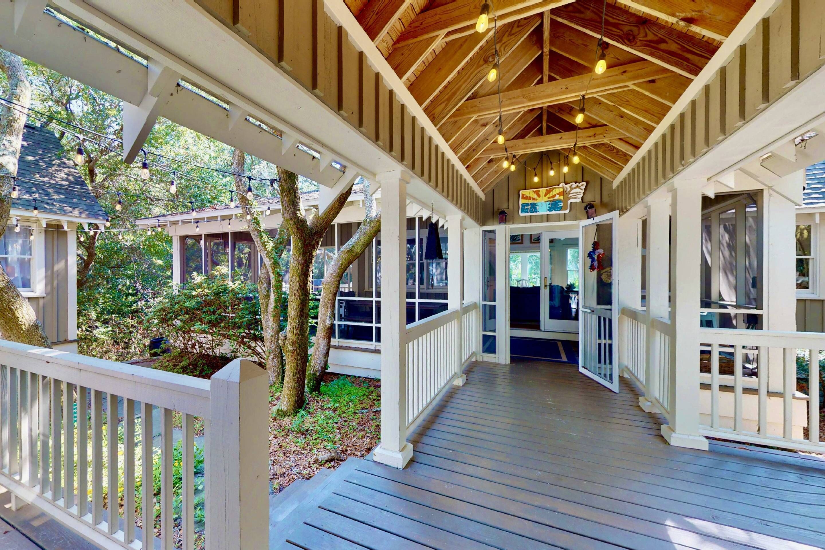 A covered wooden deck with a railing, leading to a glass door entrance.