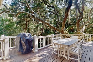 Eine Holzterrasse mit überdachtem Grill, weißen Geländern sowie einem Tisch und Stühlen.