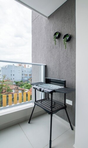 A balcony with a black grill table, a grey textured wall, and two small potted plants.