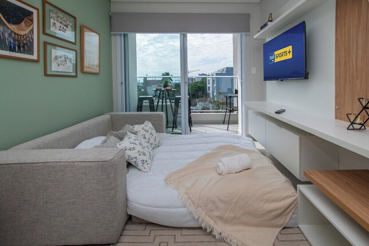 A modern living room with a sofa, a TV, and a balcony with a table and chairs.