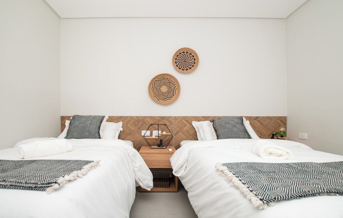 A hotel room with two beds, a wooden headboard, a nightstand with a lamp, and two wall art pieces.