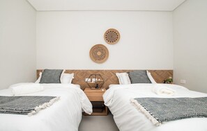 Hotellihuone, jossa on kaksi sänkyä, puinen pääty, yöpöytä lampun kanssa ja kaksi seinätaideteosta.