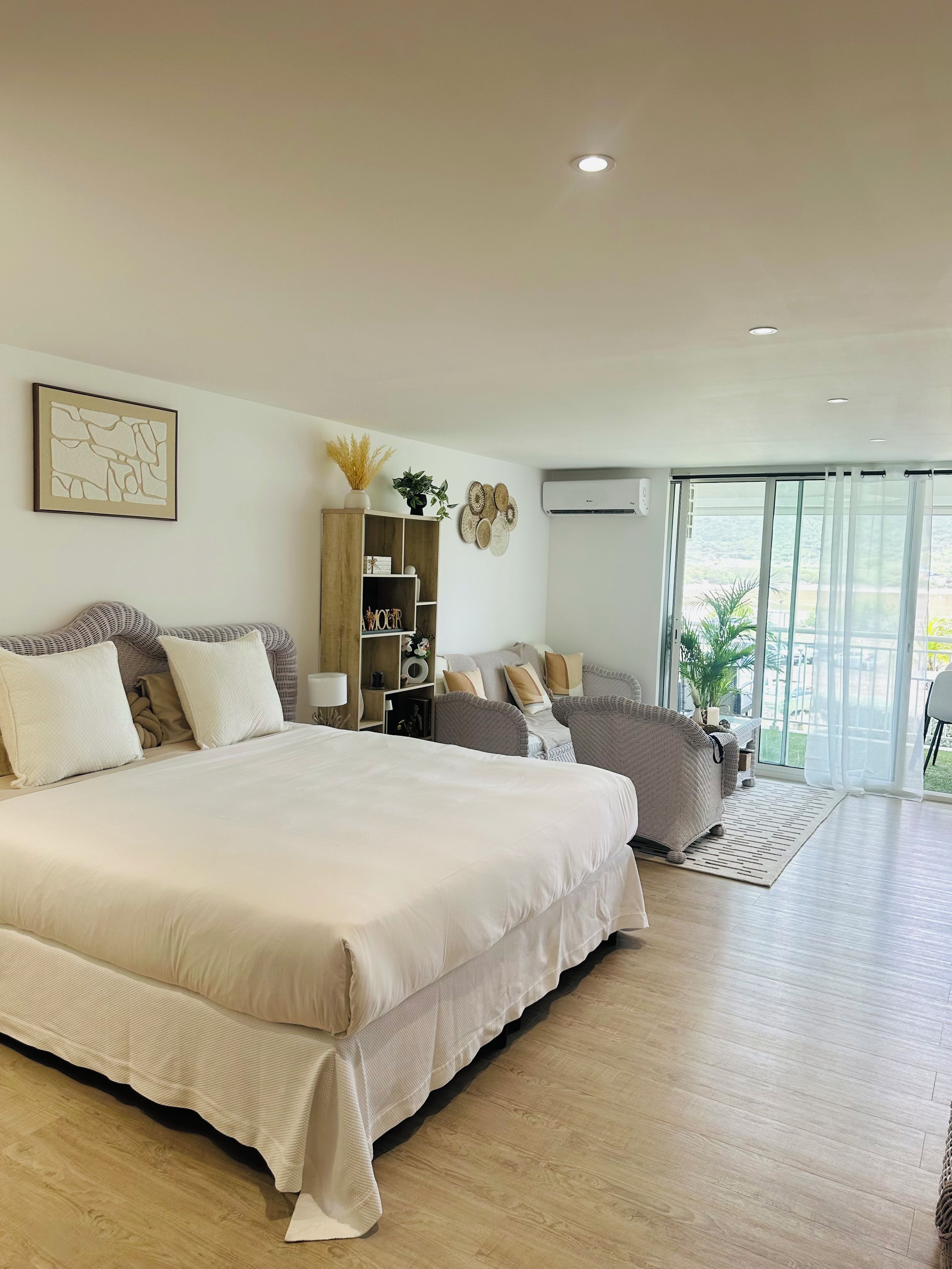 Un dormitorio amplio con una cama grande, una mesita de noche de madera y vistas al exterior a través de una puerta corrediza de vidrio.