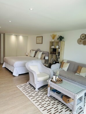 A bedroom with a bed, a white armchair, a grey sofa, and a wicker coffee table. - Bohemian studio just a stone's throw from the beach (Mont vernon)