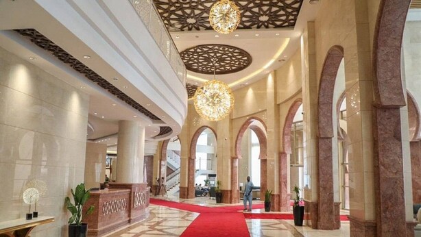 Un vestíbulo espacioso con alfombra roja, grandes columnas e iluminación decorativa en el techo.
