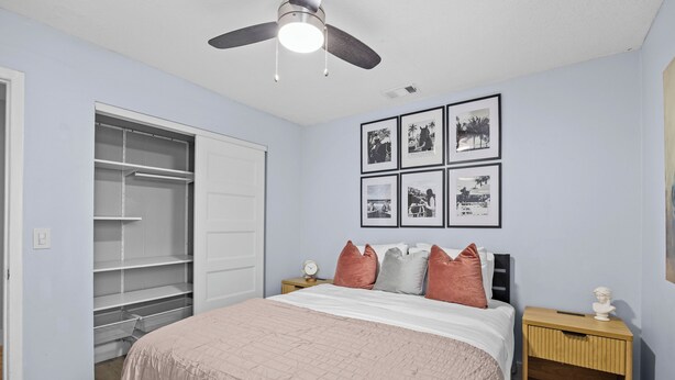 Une chambre à coucher comprenant un lit, une table de chevet, une commode, un placard et un ventilateur de plafond.