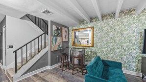 Un escalier au design moderne, un canapé de couleur turquoise et un mur orné d’un motif de feuilles tropicales.
