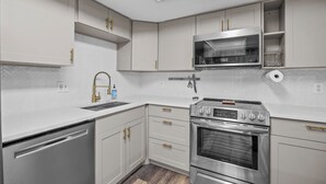 Une cuisine moderne dotée d’appareils électroménagers en acier inoxydable, de meubles blancs et d’un dosseret de carrelage disposé en motif chevrons.