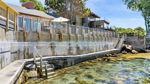 A concrete retaining wall with steps leading down to a clear water body, surrounded by buildings with large windows and a wooden fence. - Stay at Windward Point (Gloucester)