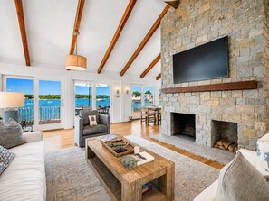 Amplia sala de estar con chimenea de piedra, televisor de pantalla plana en la pared y vista al mar a través de amplios ventanales.
