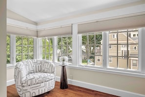 A room with large windows, a patterned armchair, and a small table with a vase.