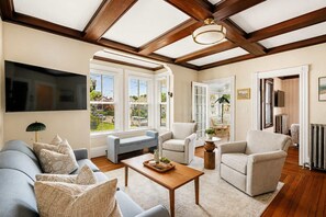 A spacious living room with a high ceiling, large windows, and a fireplace.