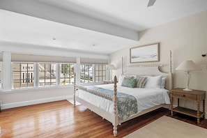A bedroom with a large window, a bed, a nightstand, and a lamp.
