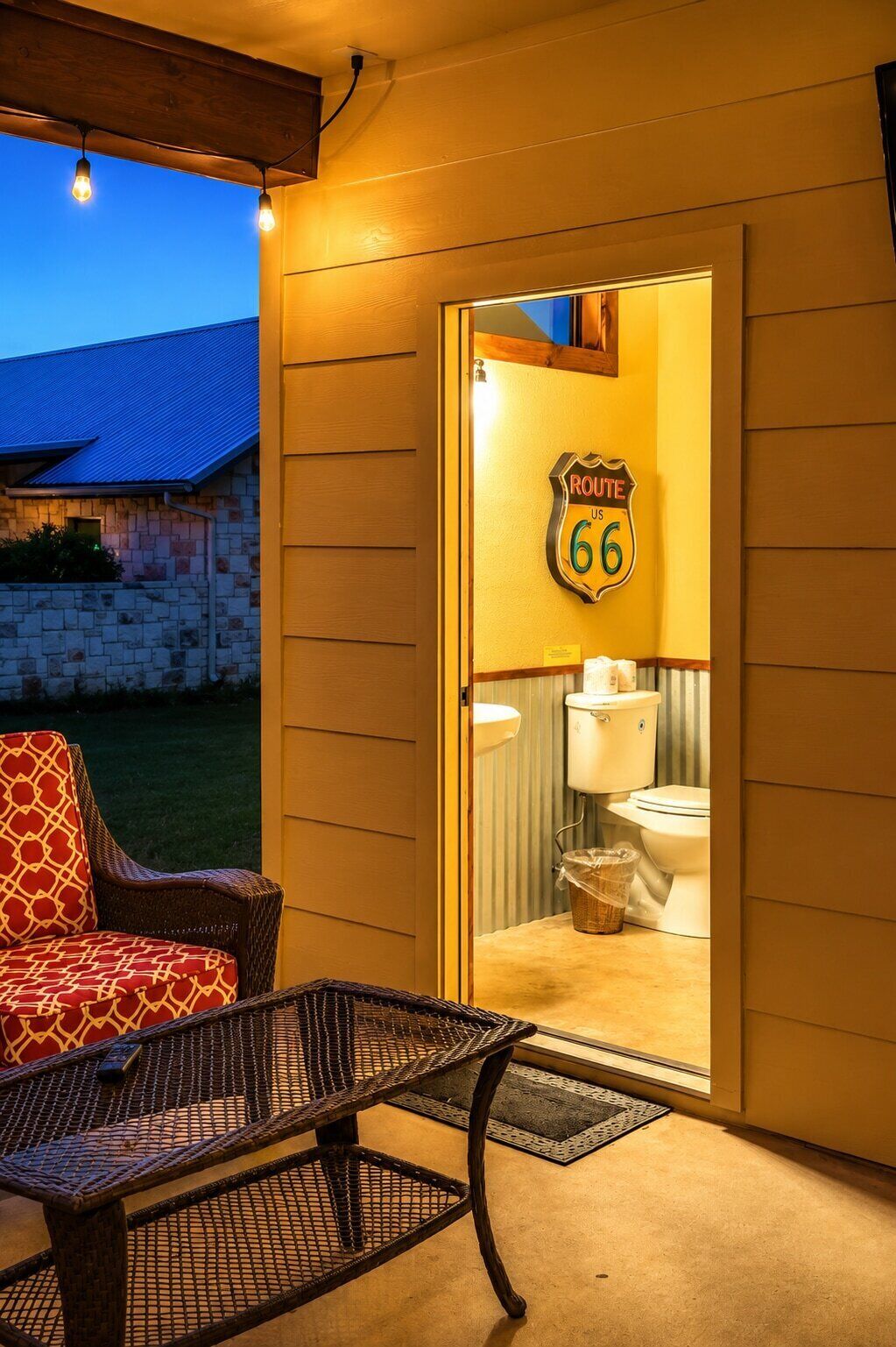 Ein Zimmer mit Blick auf ein blaues Gebäude, eine Tür mit Route 66 Schriftzug, ein Korbstuhl und ein Metalltisch.