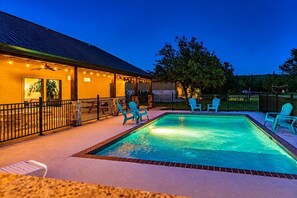 Una piscina con zona delimitada por valla, sillas de descanso y un edificio con luces colgantes.