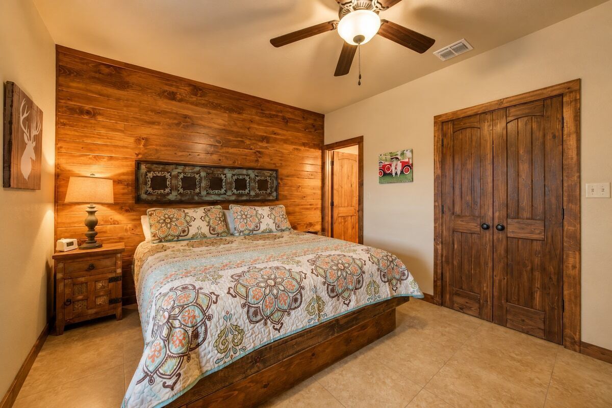 Ein Schlafzimmer mit Holz-Kopfteil, einem Bett mit gemusterten Betttextilien, einem Nachttisch mit Lampe und einem Holzschrank.