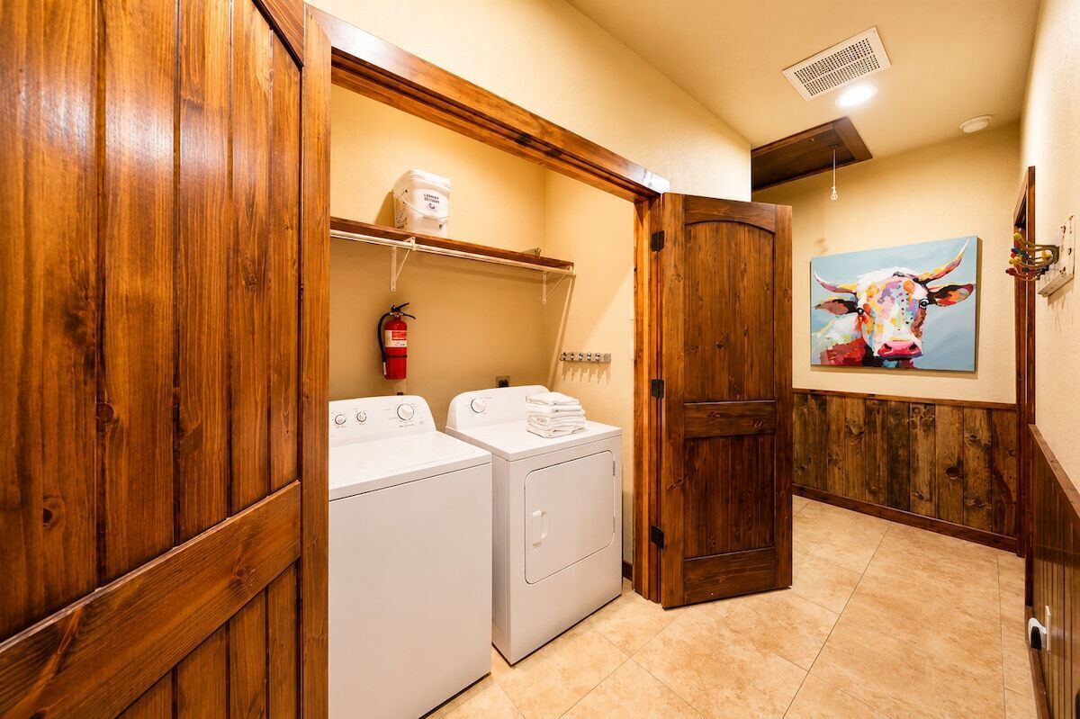A laundry room with two white washers and dryers, a fire extinguisher on the wall, and a wooden door.