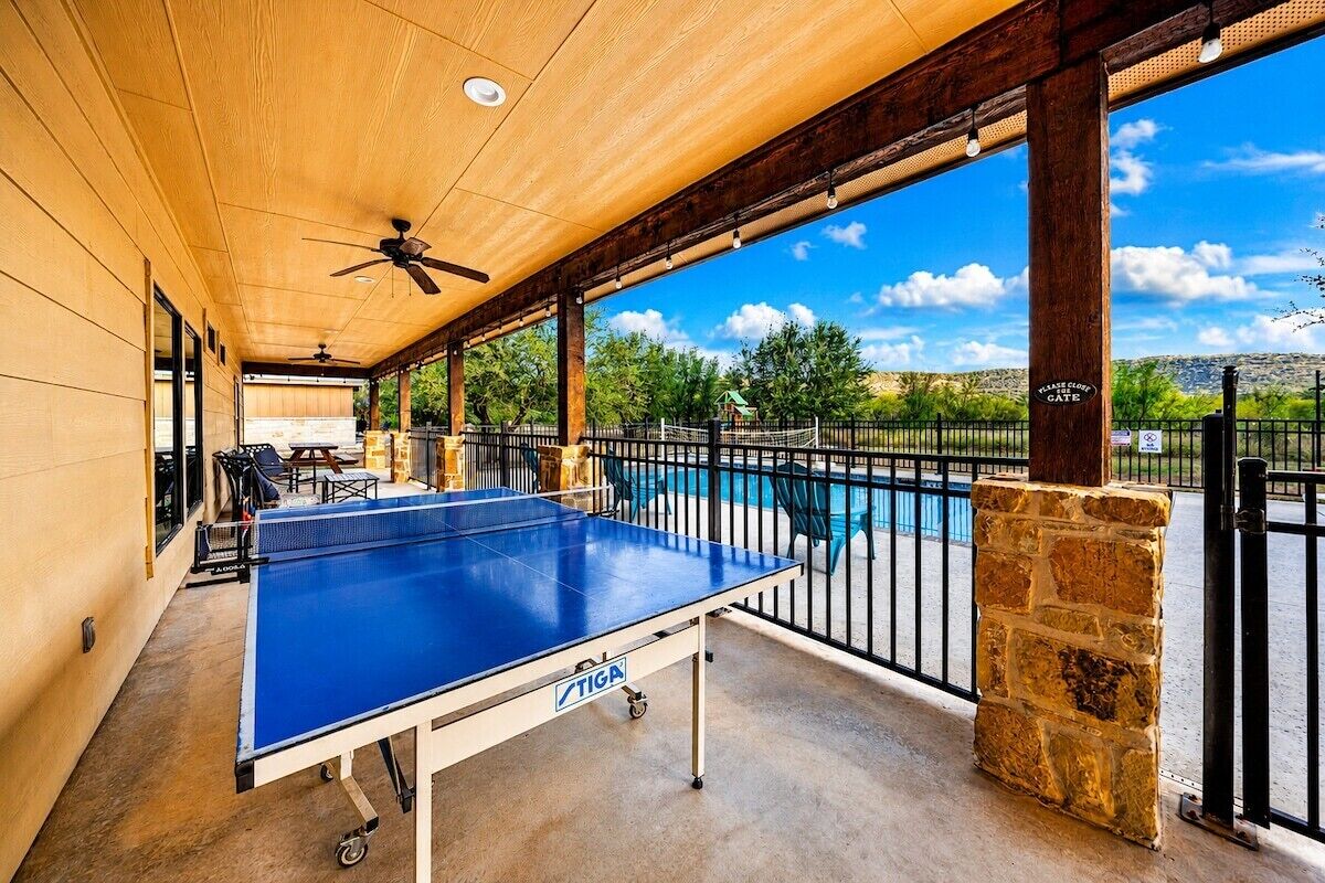 Une table de ping-pong d’extérieur de la marque TIGA, un ventilateur de plafond et une vue sur une piscine et une porte.