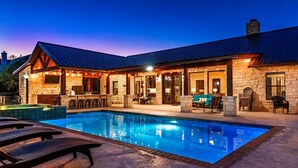 A poolside area with a stone building, outdoor seating, and a clear blue pool. - Spacious Lodge w/ Pool & Hot Tub Near Frio River (Concan)