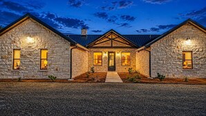 A stone house with a central entrance, two side wings, and a gravel driveway. - Spacious Lodge w/ Pool & Hot Tub Near Frio River (Concan)