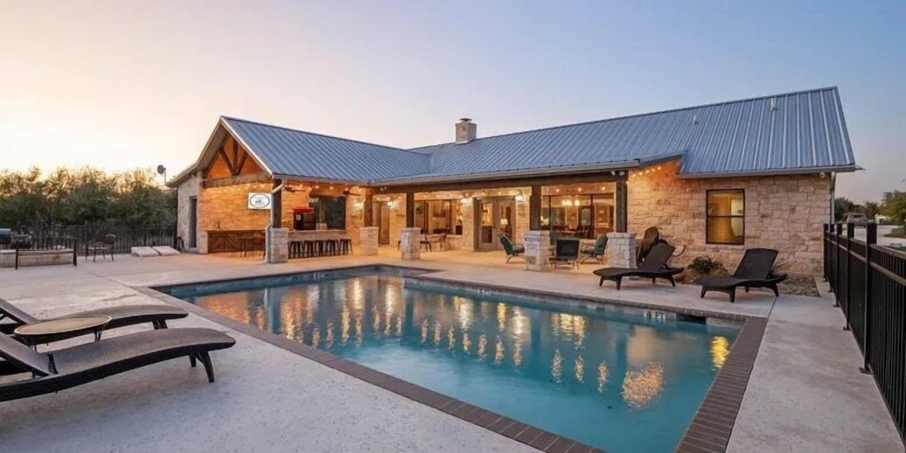 A poolside area with lounge chairs, a bar, and a stone building with a metal roof.