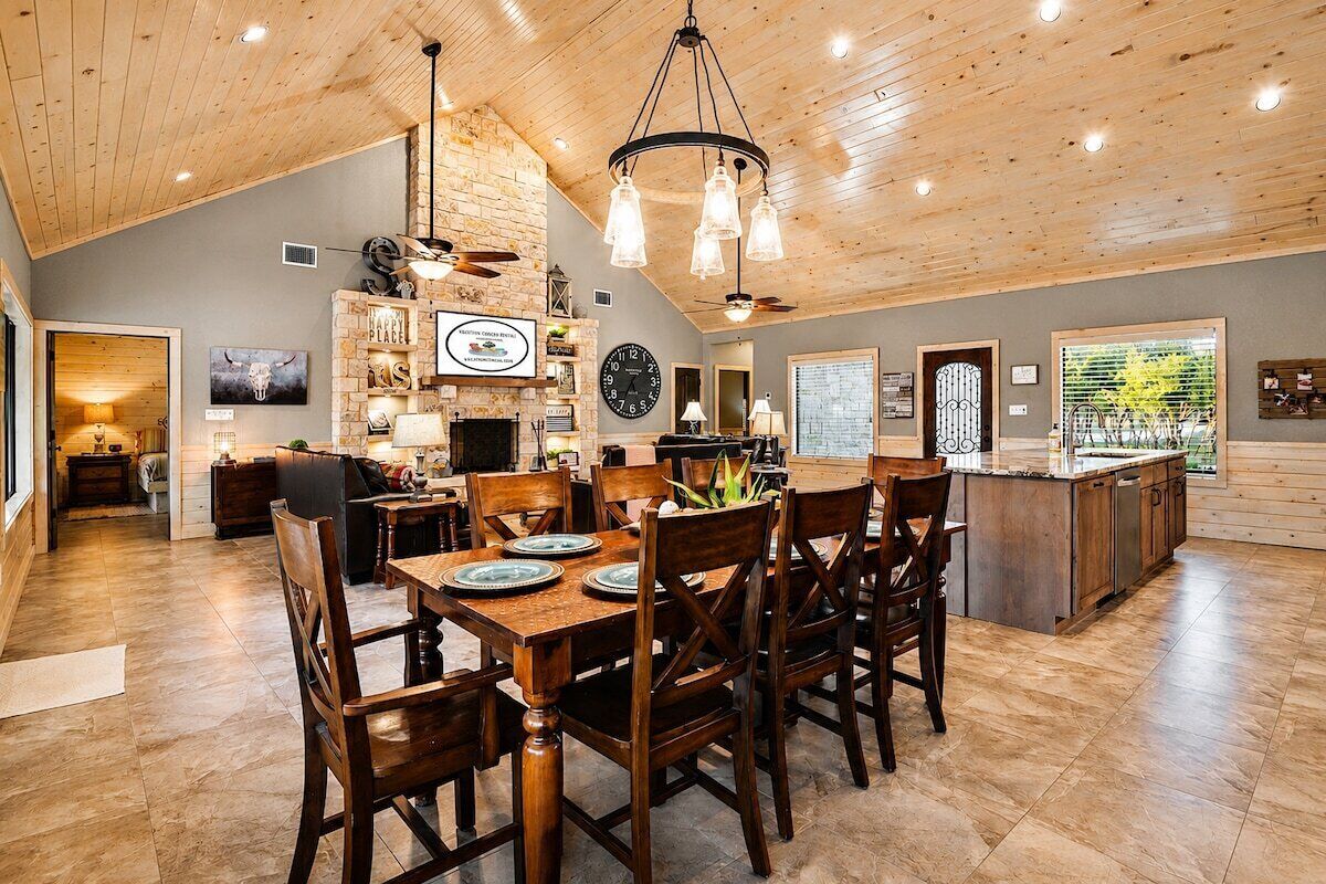 A spacious dining area with a wooden table and chairs, a stone wall with a clock, and a view of the outdoors through a window.