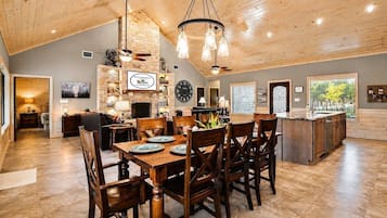 A spacious dining area with a wooden table and chairs, a stone wall with a clock, and a view of the outdoors through a window.
