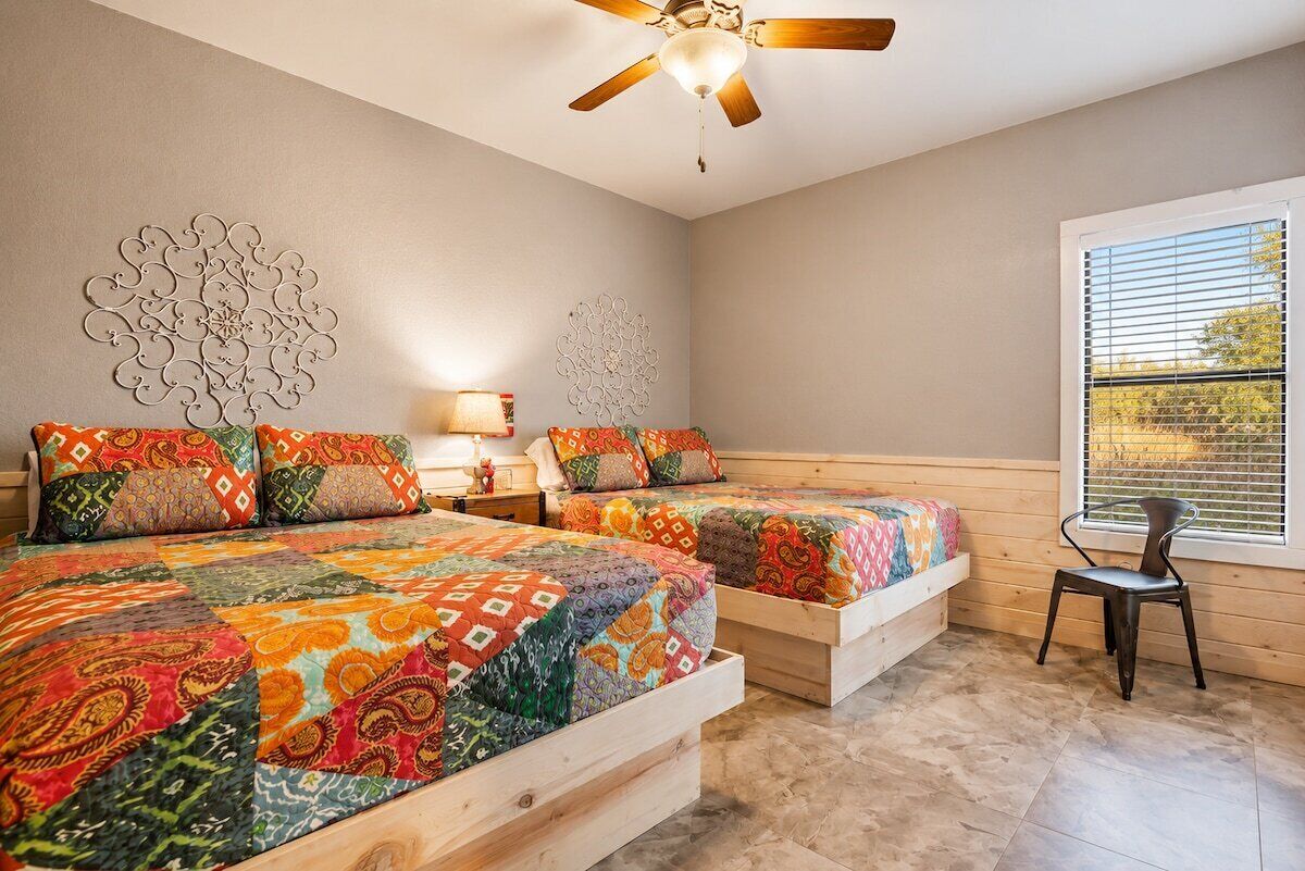 A bedroom with two wooden beds, a ceiling fan, decorative wall art, a window with blinds, and a chair.