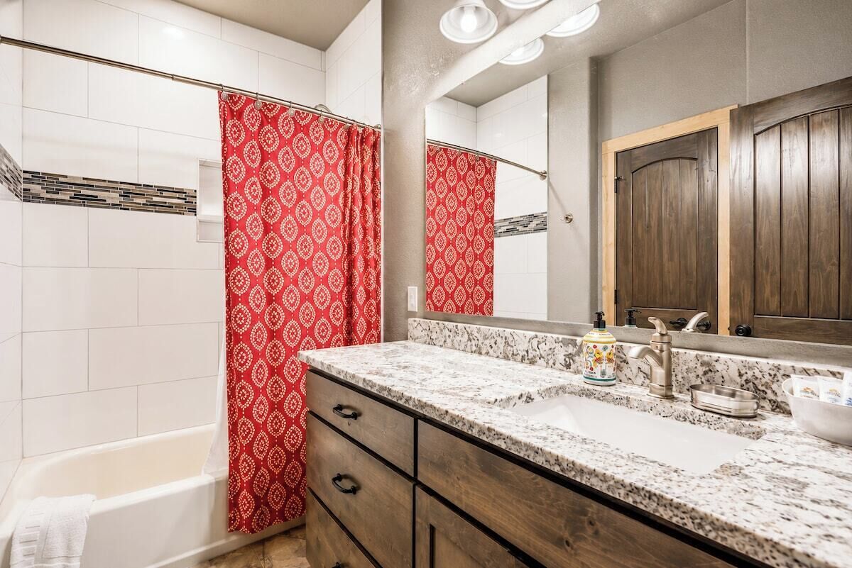 A bathroom with a shower curtain, a bathtub, a vanity with a sink, and a mirror.