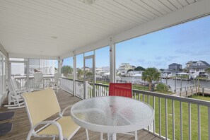 A covered outdoor area with a round table and chairs, overlooking a marina with boats. - Canalfront dock and screened porch (Surf City)