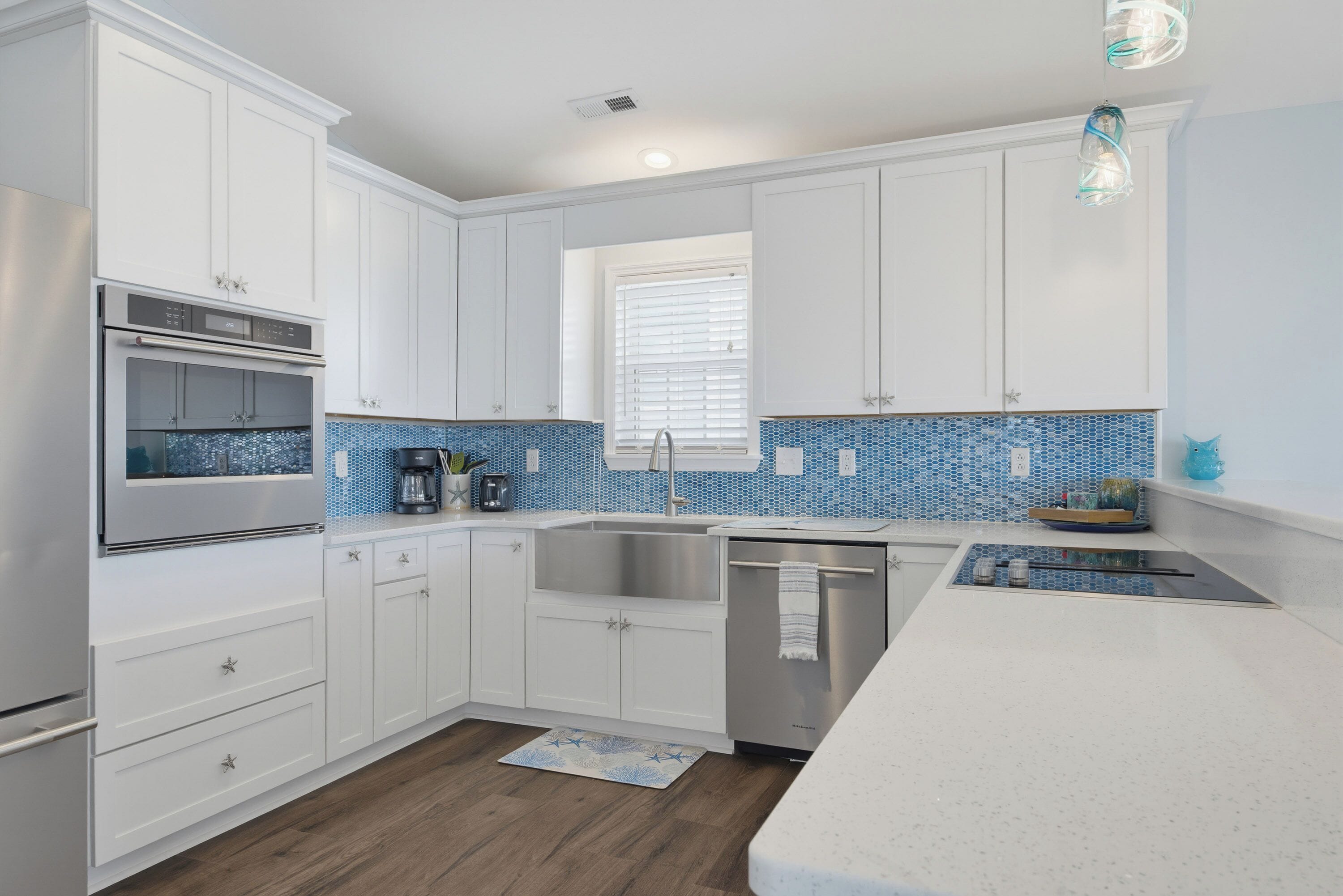 A modern kitchen with white cabinetry, a stainless steel dishwasher, and a blue-tiled backsplash.