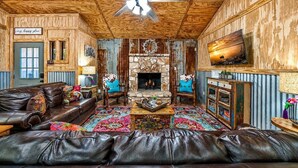 Ein gemütliches Wohnzimmer mit Kamin, Ledersofas, Fernseher und Deckenventilator.