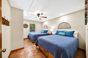 Une chambre d’hôtel avec deux lits, un ventilateur de plafond et des œuvres d’art décoratives au mur.