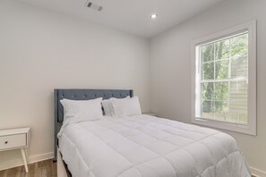 Een slaapkamer met een enkel bed, een nachtkastje, een raam met jaloezieën en een ventilatie rooster.